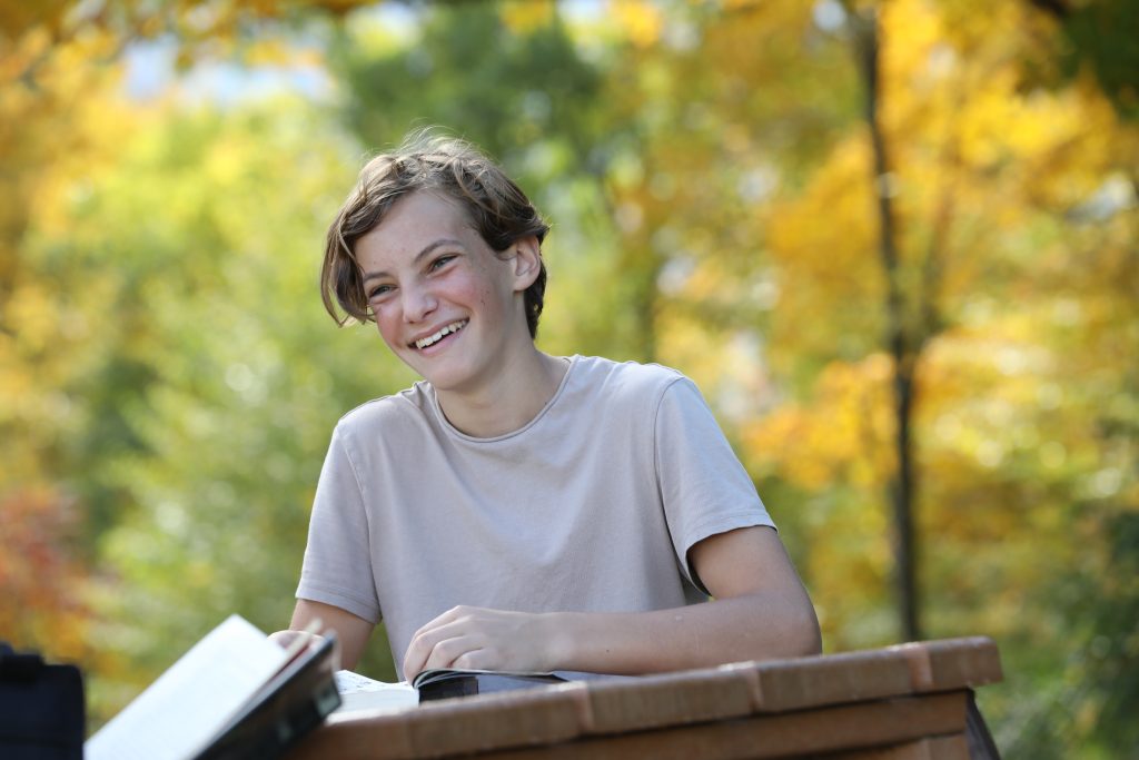 An Upper School student grins with a book outdoors