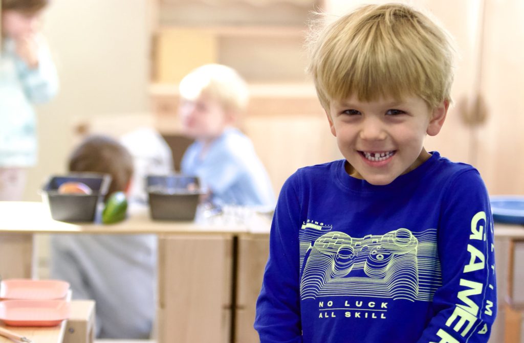A Pre-K student grins in front of a bright classroom