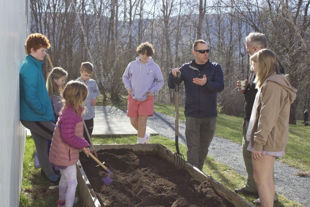 Parents and students hold tools around a raised garden bed with freshly turned soil