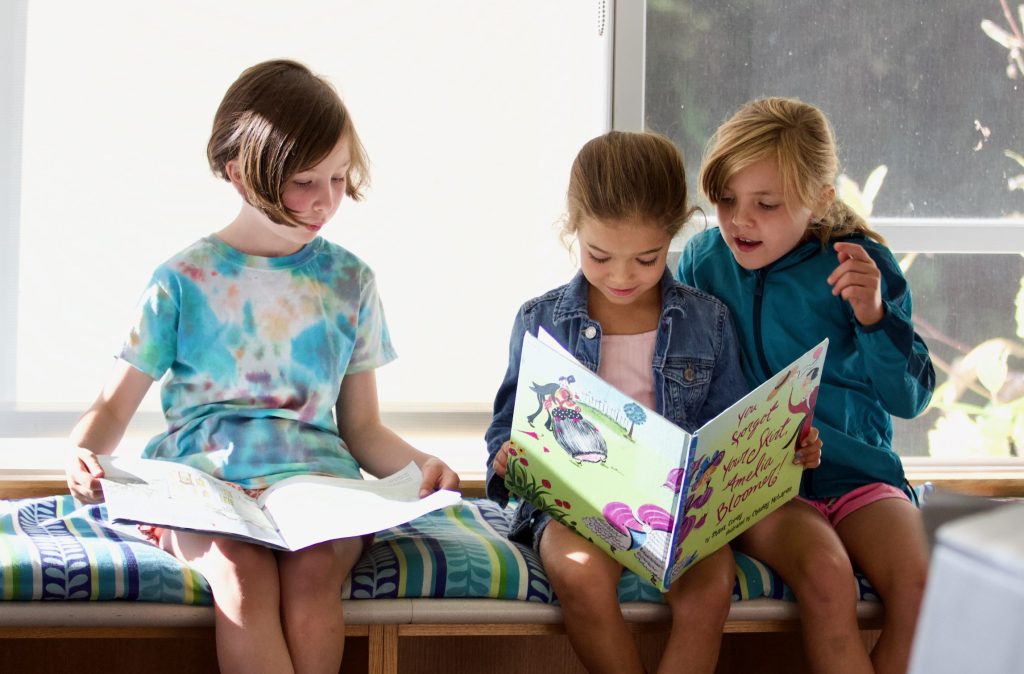 Three Lower Schoolers share a window seat to read